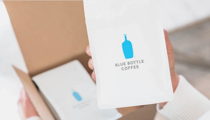 A hand holding a bag of Blue Bottle Coffee, with the shipping box in the background.