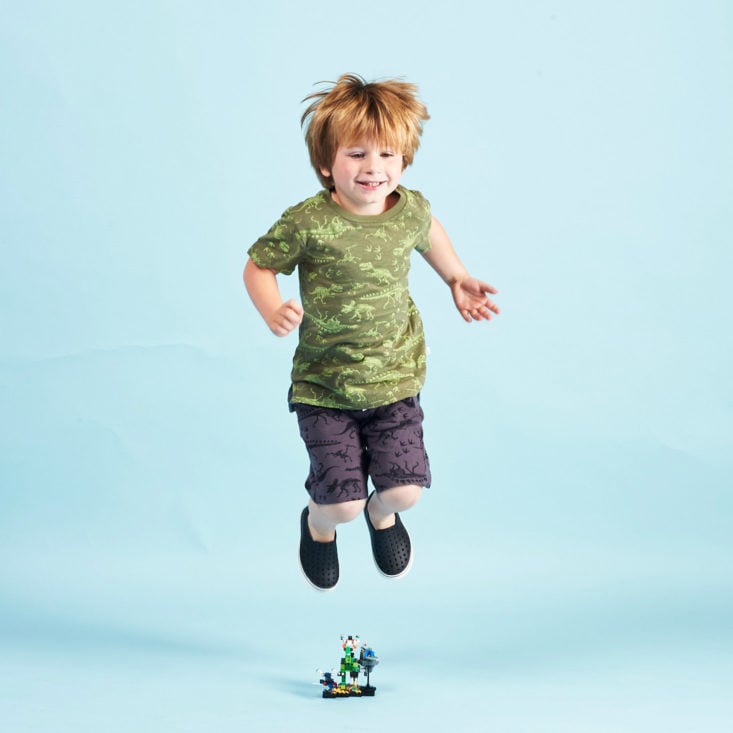 Stitch Fix Kids little boy wearing dinosaur print clothes, jumping over a toy.