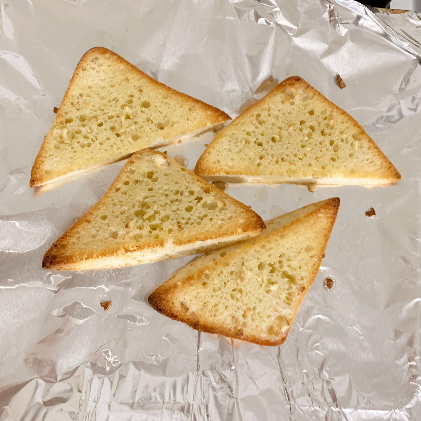 toasted triangular cut ciabatta bread with garlic and butter on baking sheet
