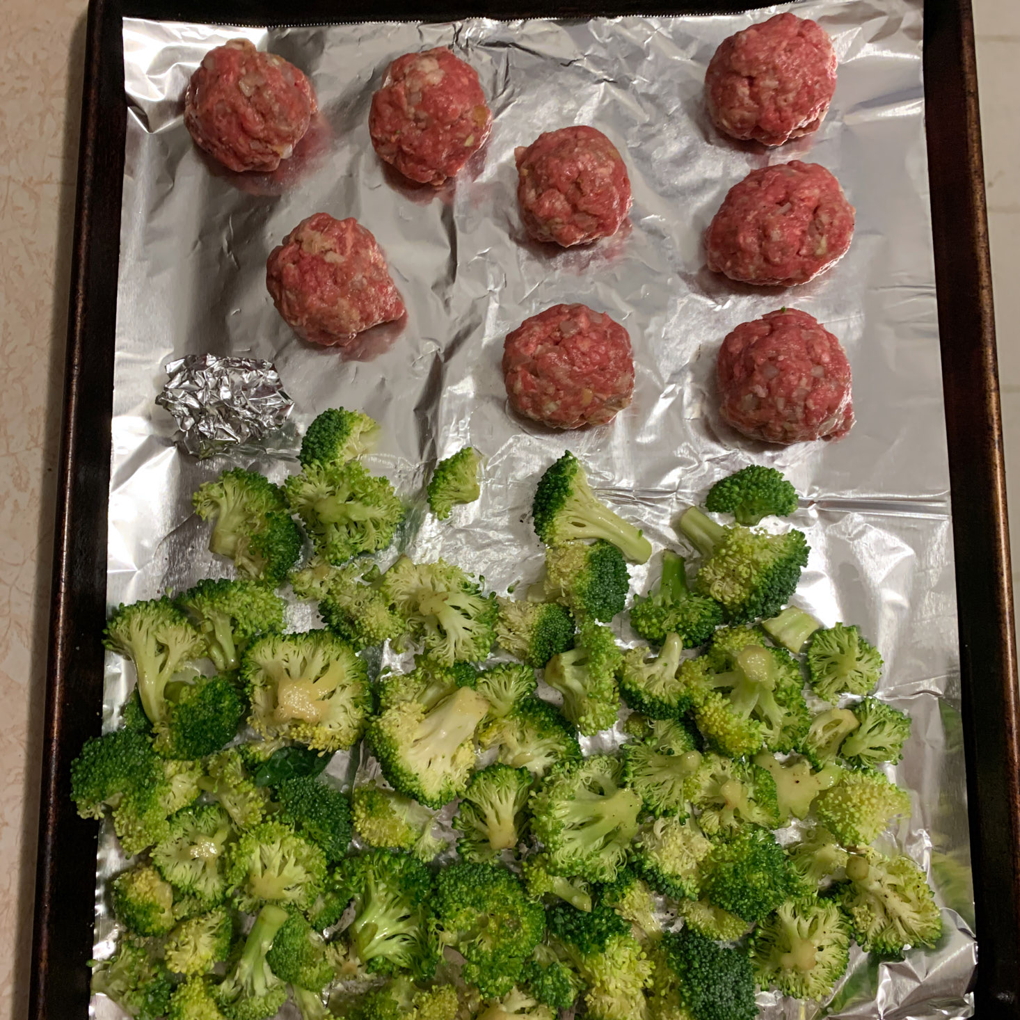 Raw formed meatballs and broccoli on baking sheet