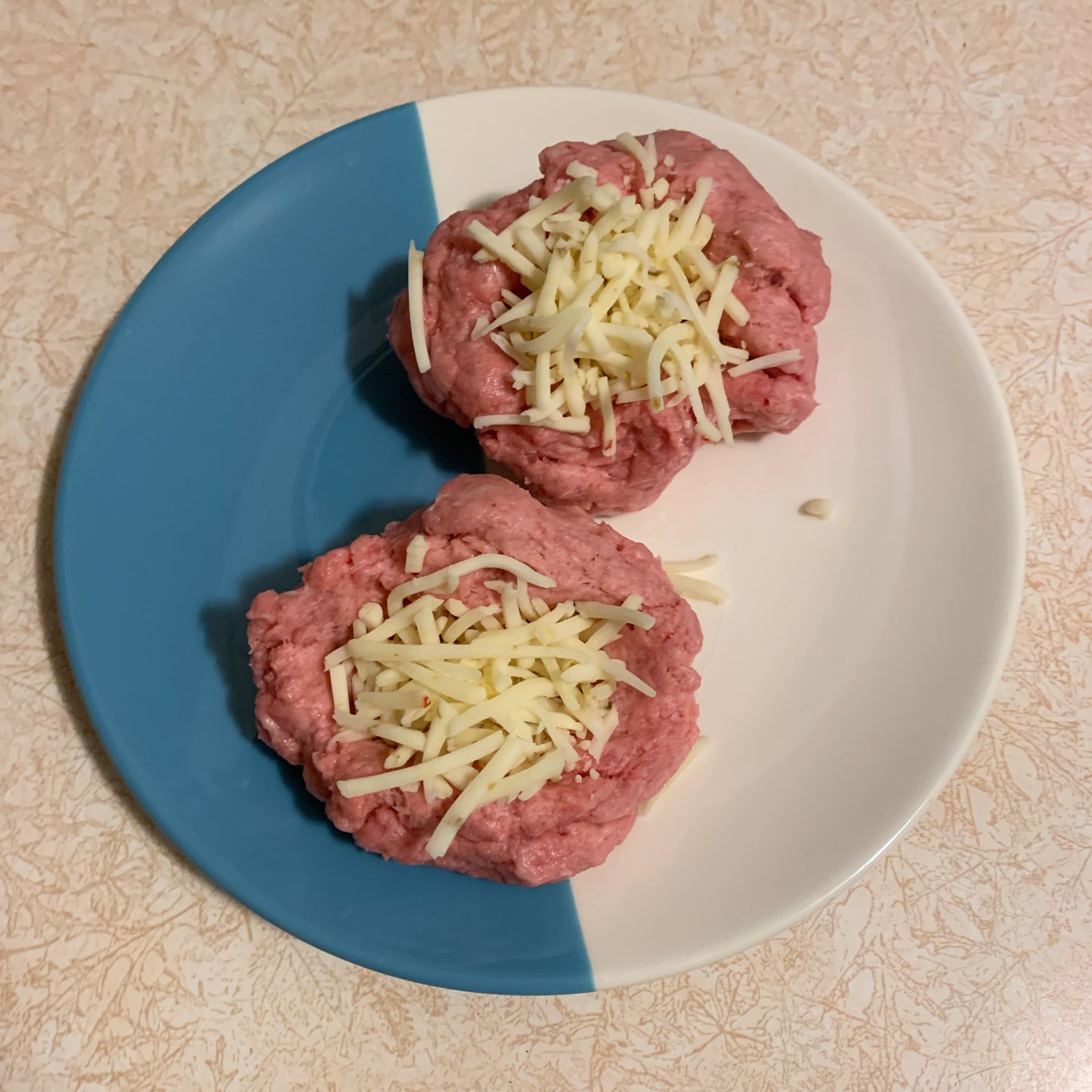 raw pork burgers with cheese about to be stuffed in on plate