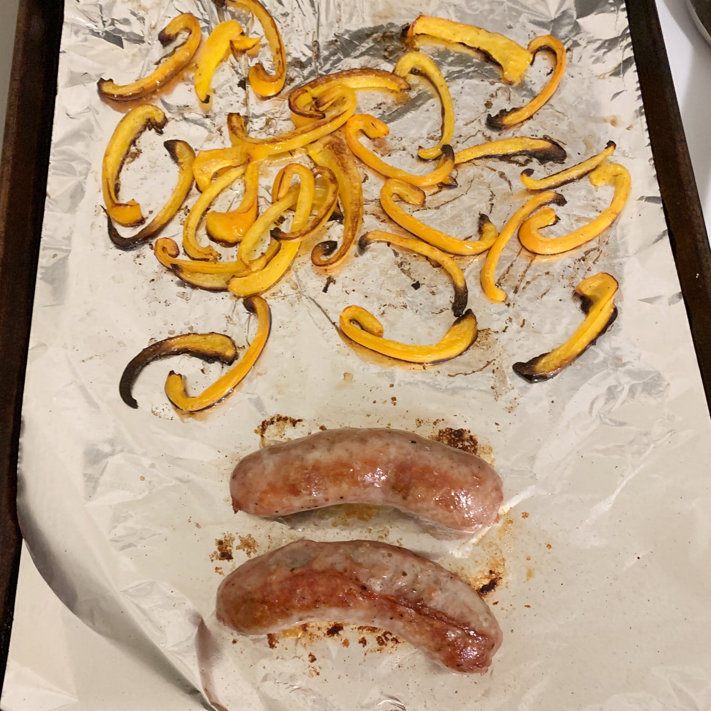 Cooked sausages and peppers on baking sheet