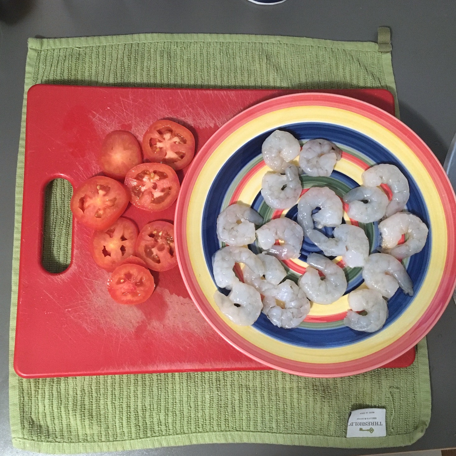 shrimp sandwich sliced tomatoes on a red cutting board and seasoned shrimp on a striped plate