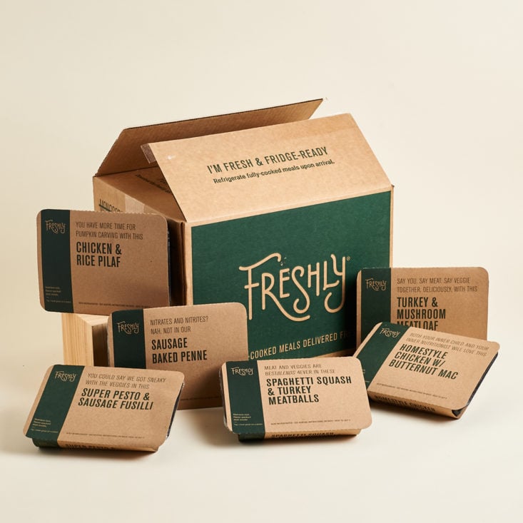 A collection of pre-packaged Freshly meals surrounding a cardboard box from Freshly.