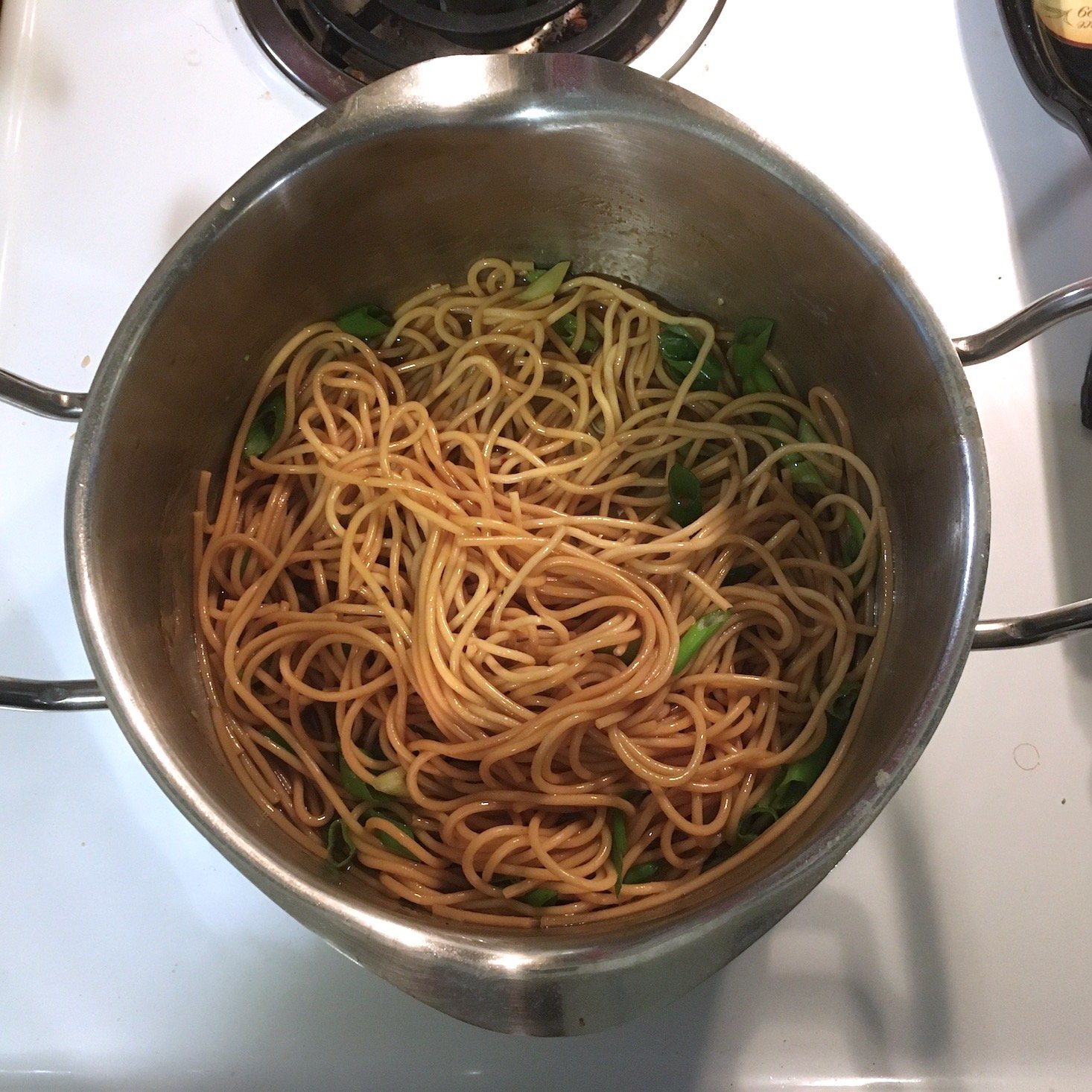 teriyaki noodles mixed with sauce and green onions in a pot