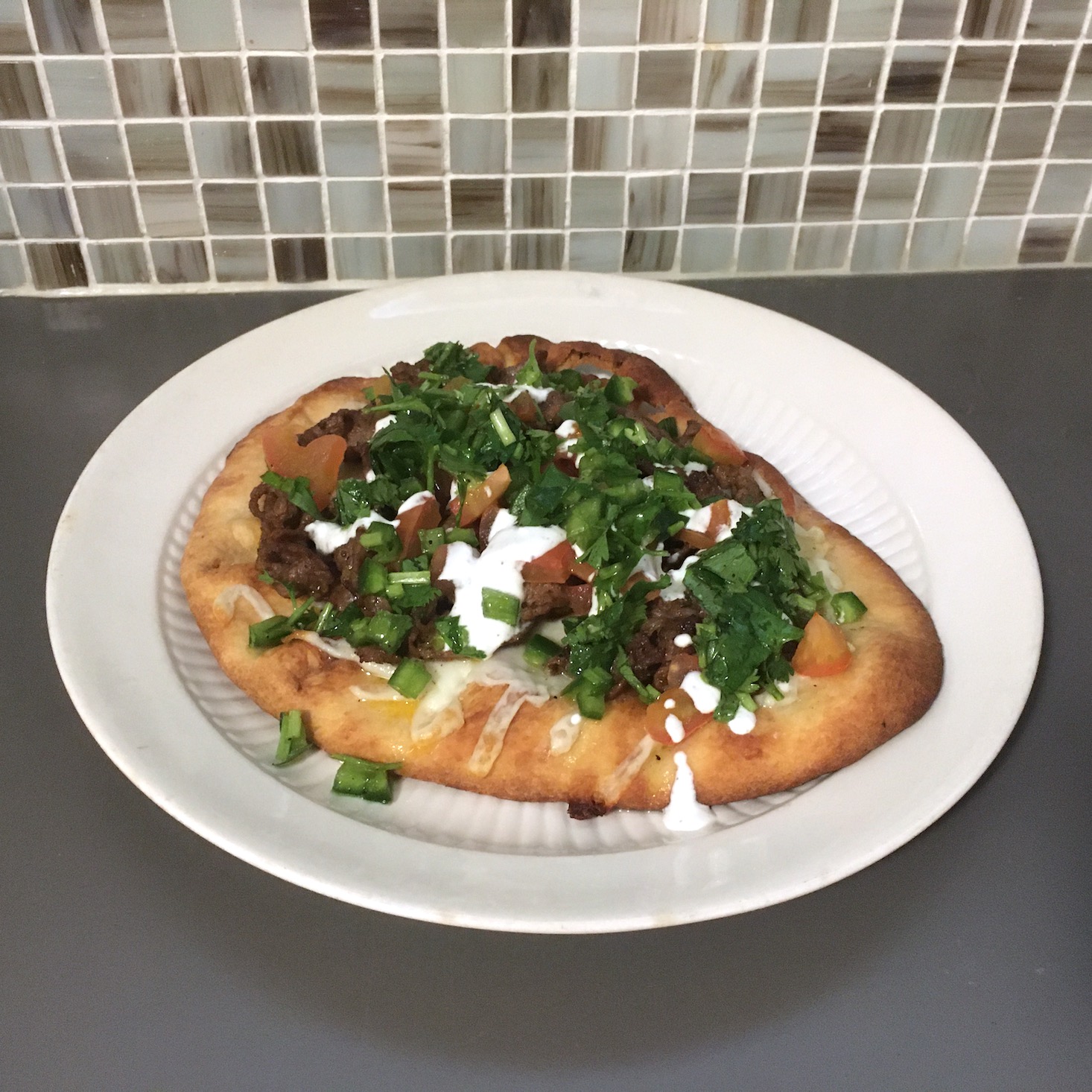 steak flatbread plated against tile backdrop on white plate, front view