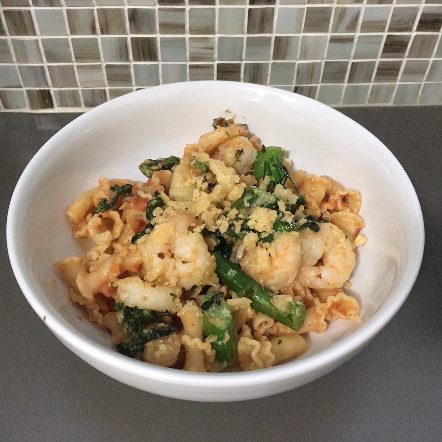 tomato shrimp pasta plated against tile backdrop