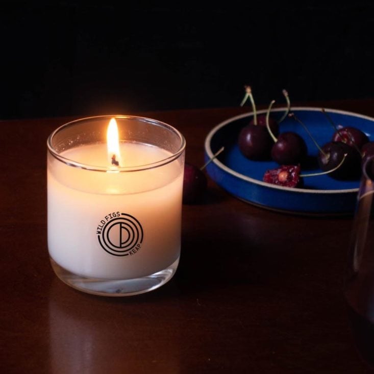 Keap candle lit next to a bowl of cherries.