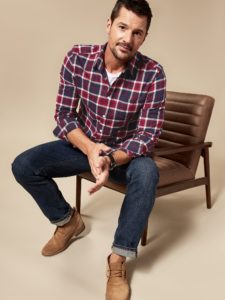 man perched on the edge of a chair wearing jeans and a flannel shirt