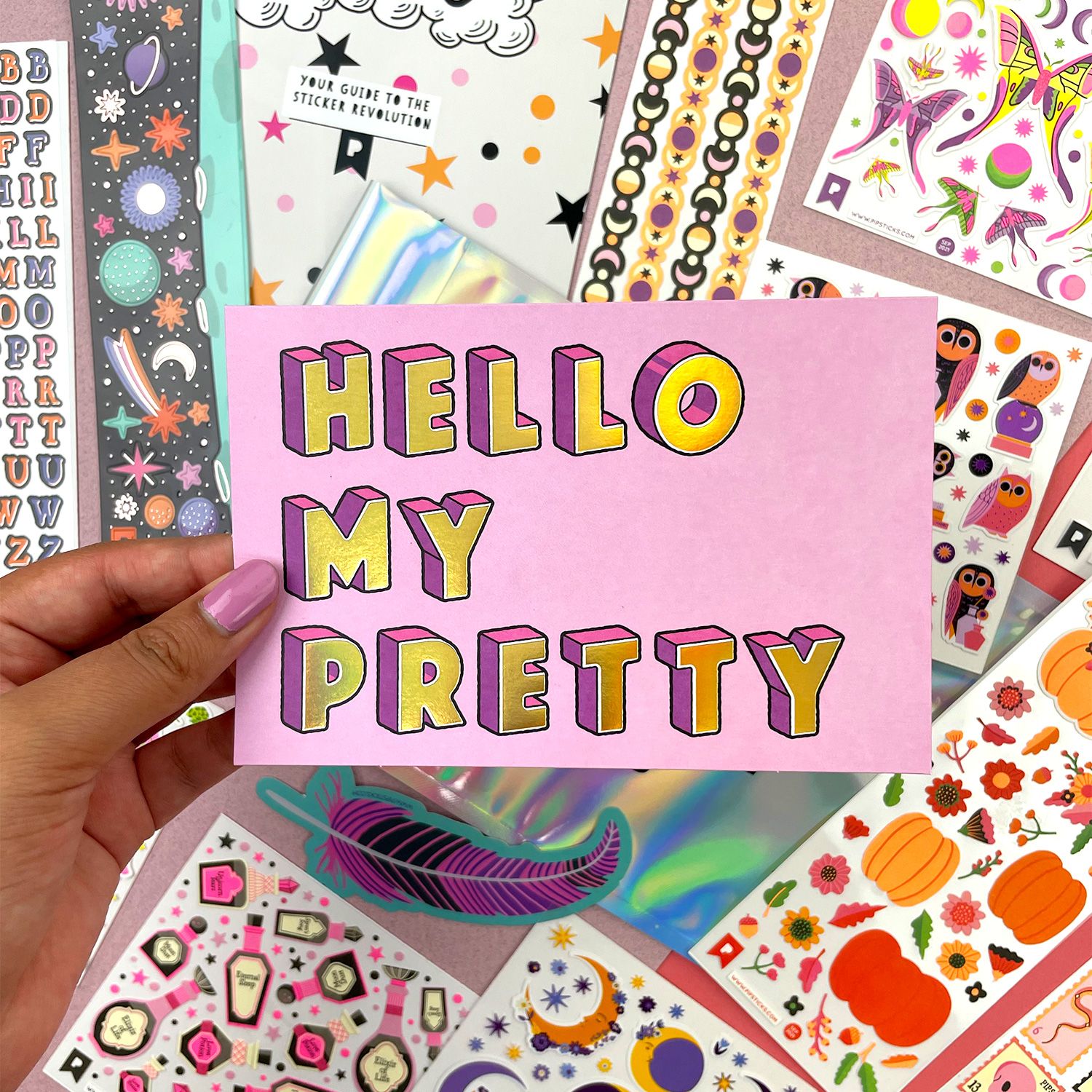 picture of "Hello My Pretty" sticker with gold lettering and purple shadowing; other stickers visible in background