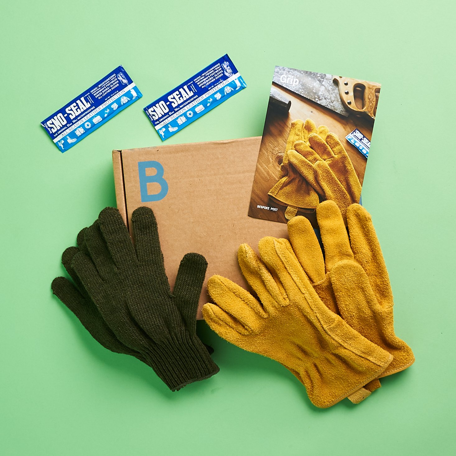 Everything in the box. Yellow Buffalo suede work gloves, brown-knit glove inserts, and two packets of waterproofing gel all atop a brown box.