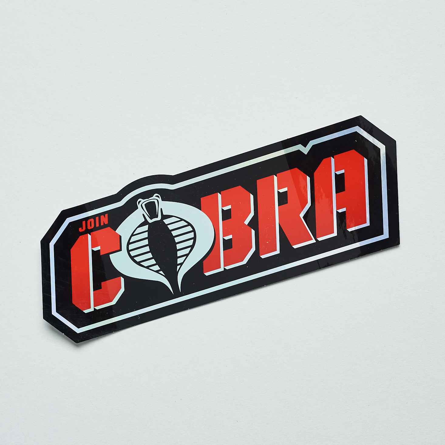 A black sticker with red lettering that says, "Join Cobra." The Cobra logo is the O in Cobra.