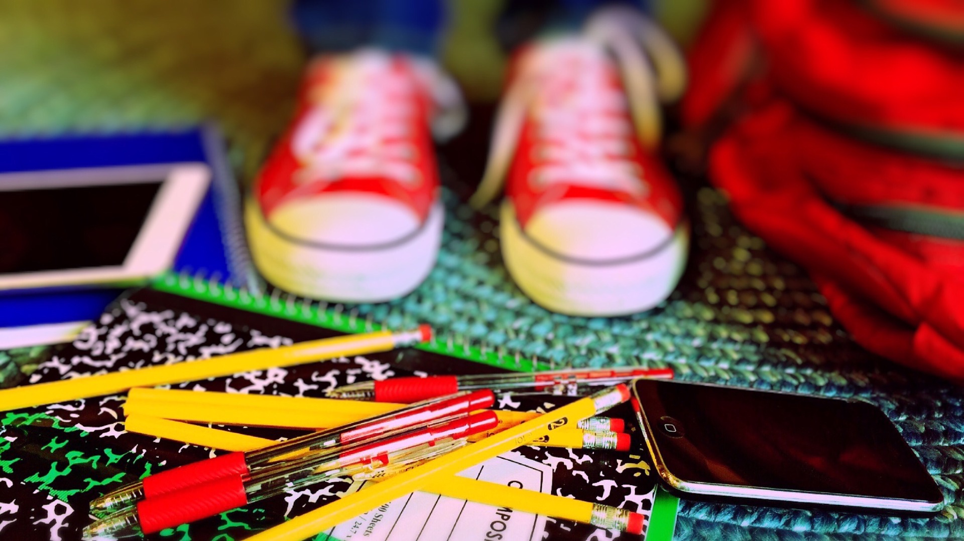 Photo of red sneakers, pens, pencils, notebooks and other back to school items