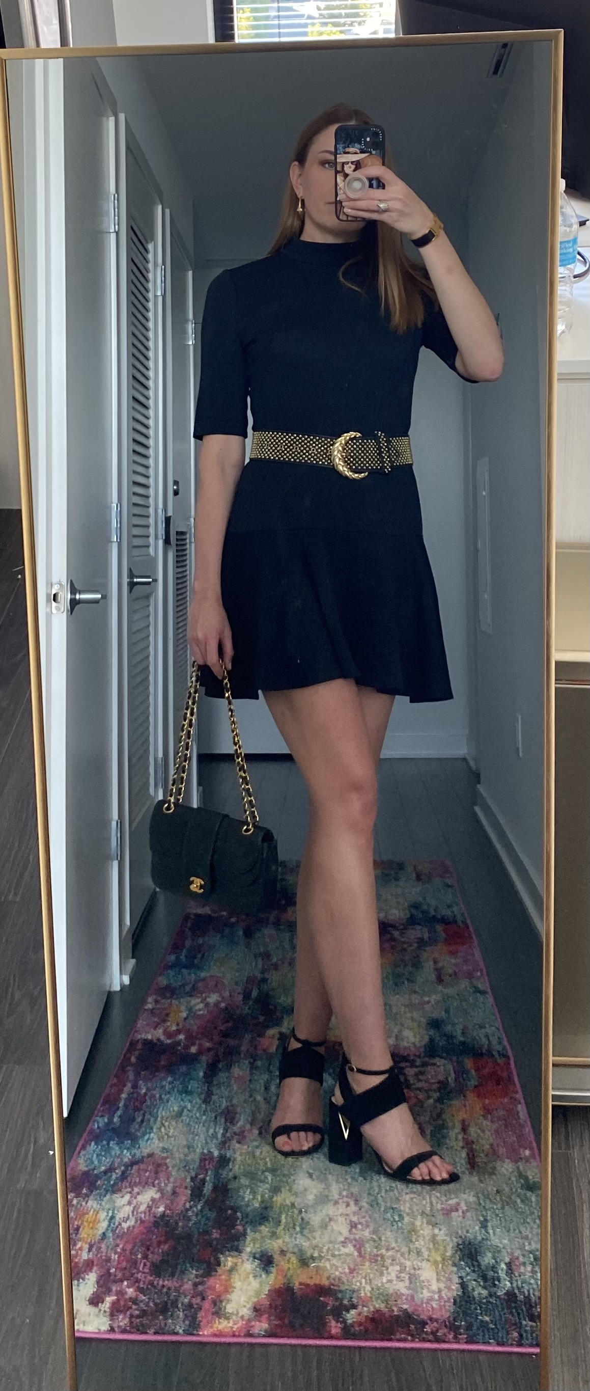 Woman in black dress with gold-tone studded leather belt and chain strap shoulder bag