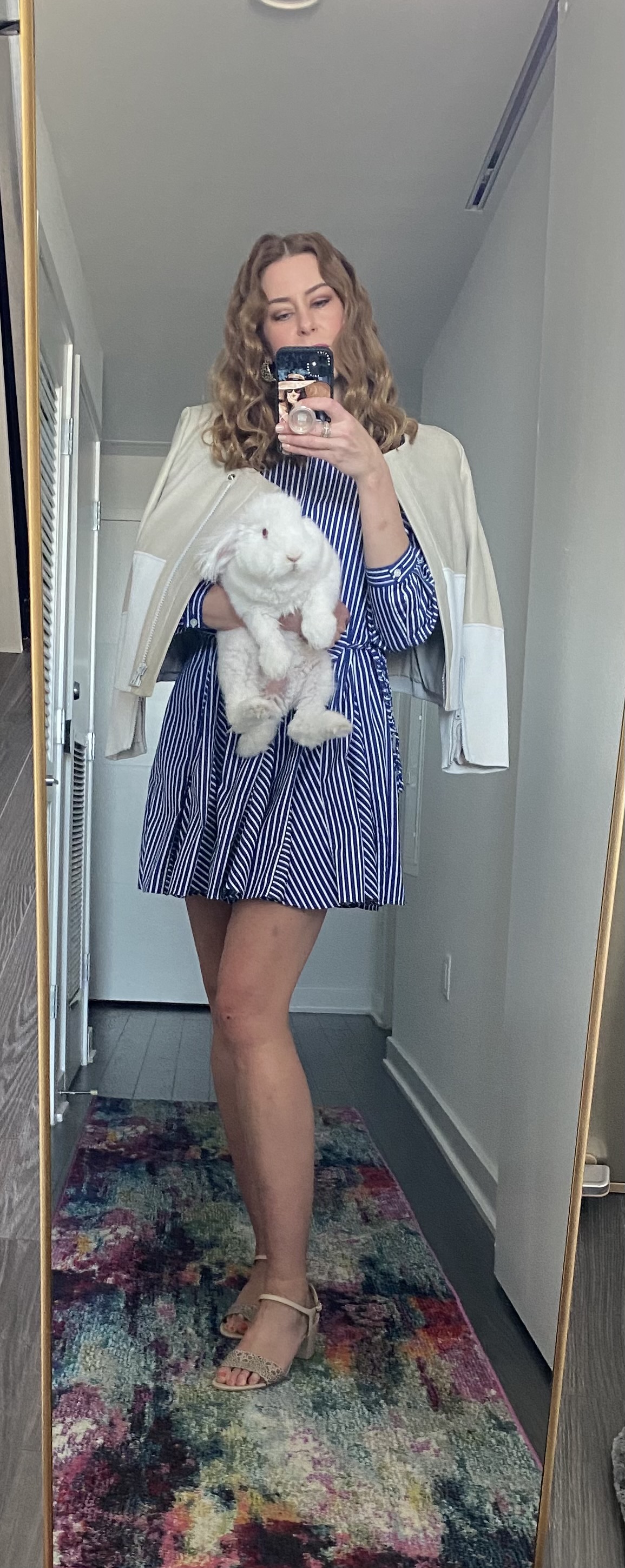 Woman in striped blue and white dress with tan and beige leather jacket holding a bunny rabbit