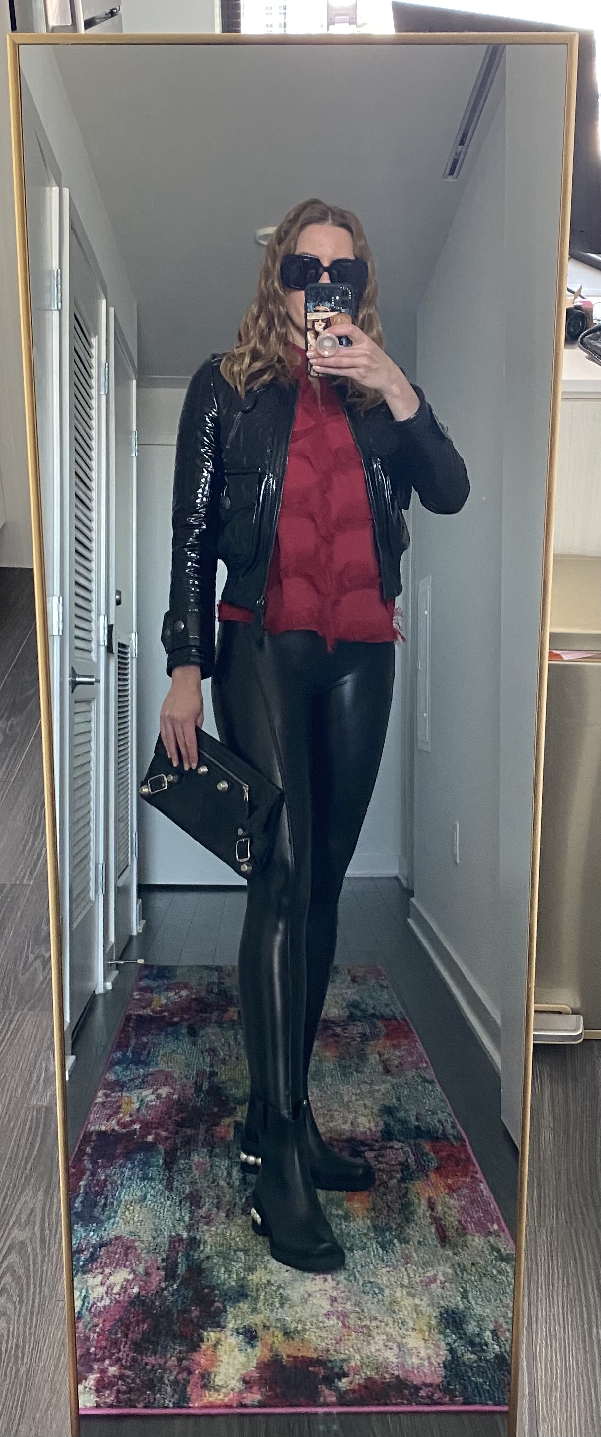 Woman in red top with black leather motorcycle jacket and shiny black faux leather leggings 