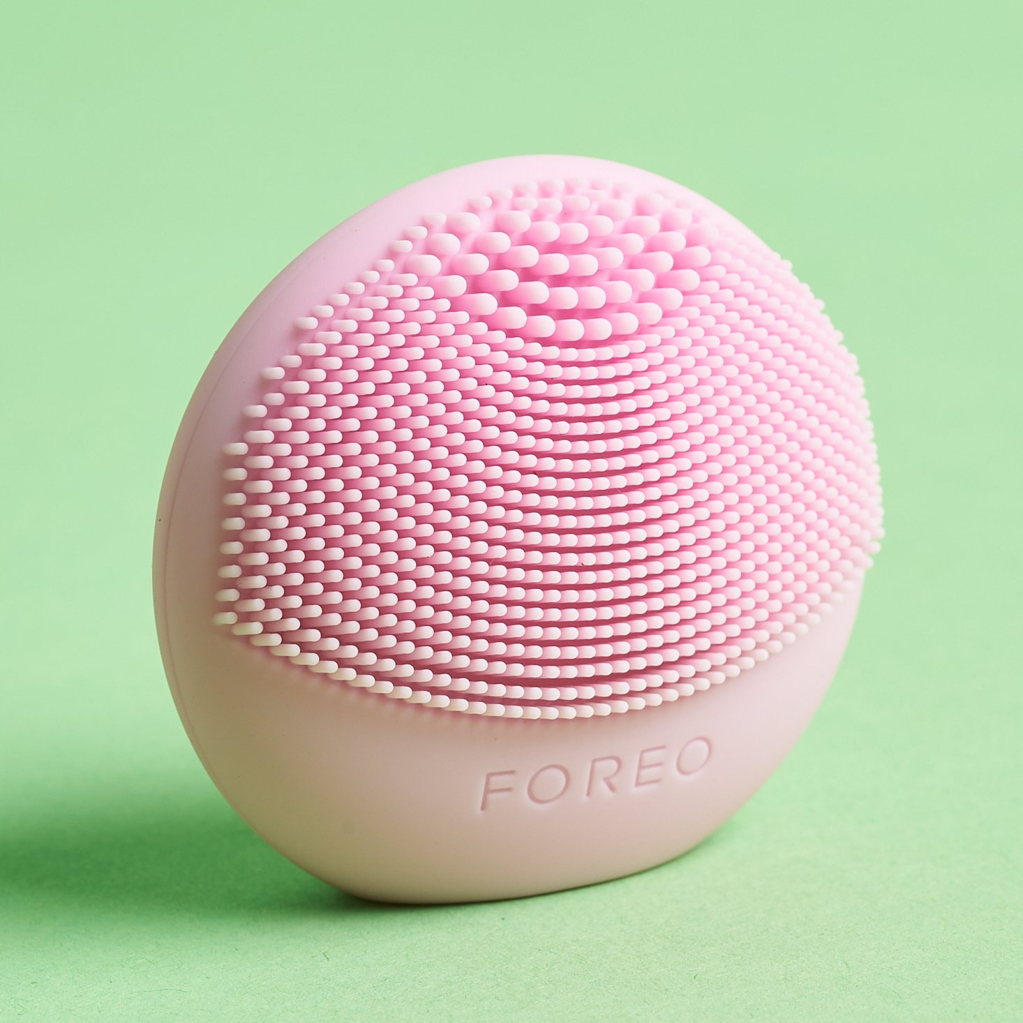 pink silicone cleansing brush on green background
