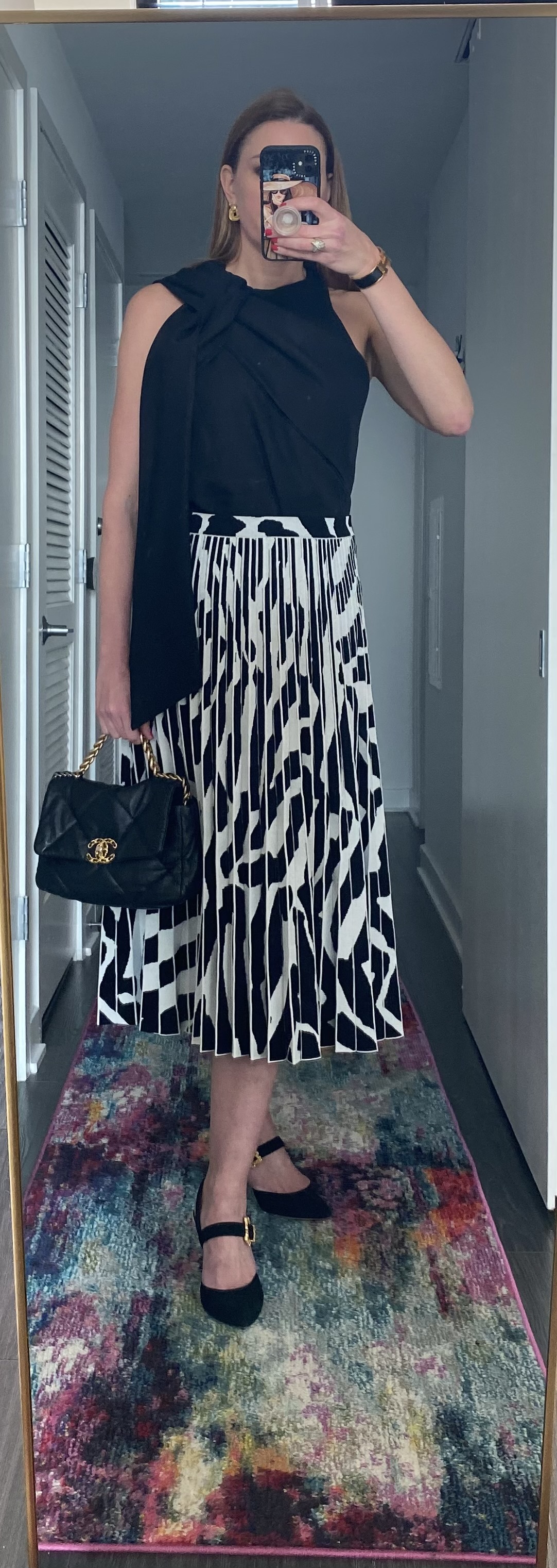 Woman wearing pleated printed skirt and draper black shirt with handbag