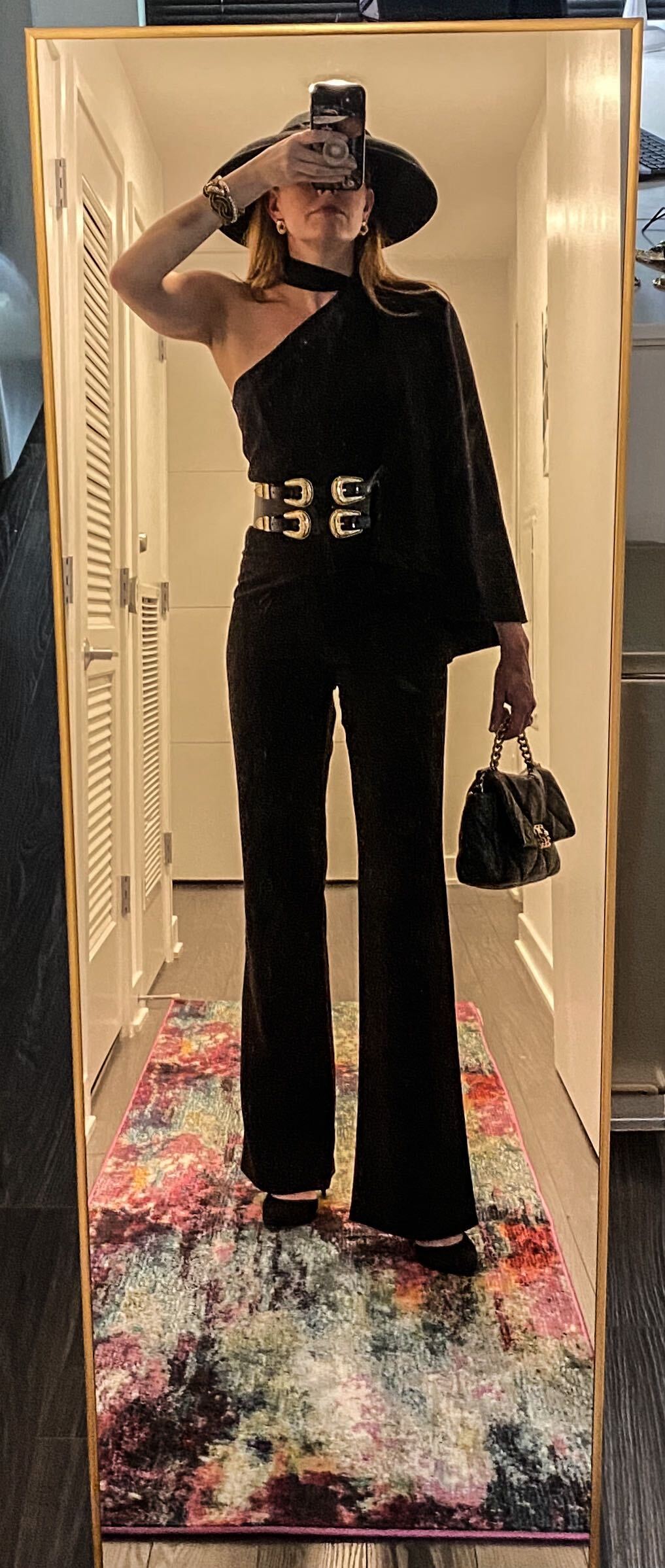 Woman in black jumpsuit with black hat, heels and handbags