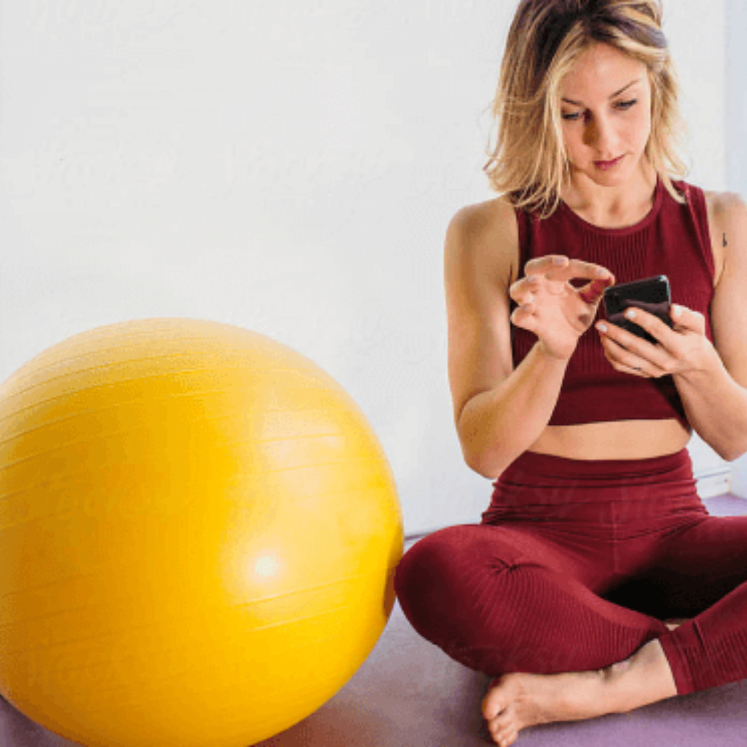 Woman sitting next to yellow exercise ball