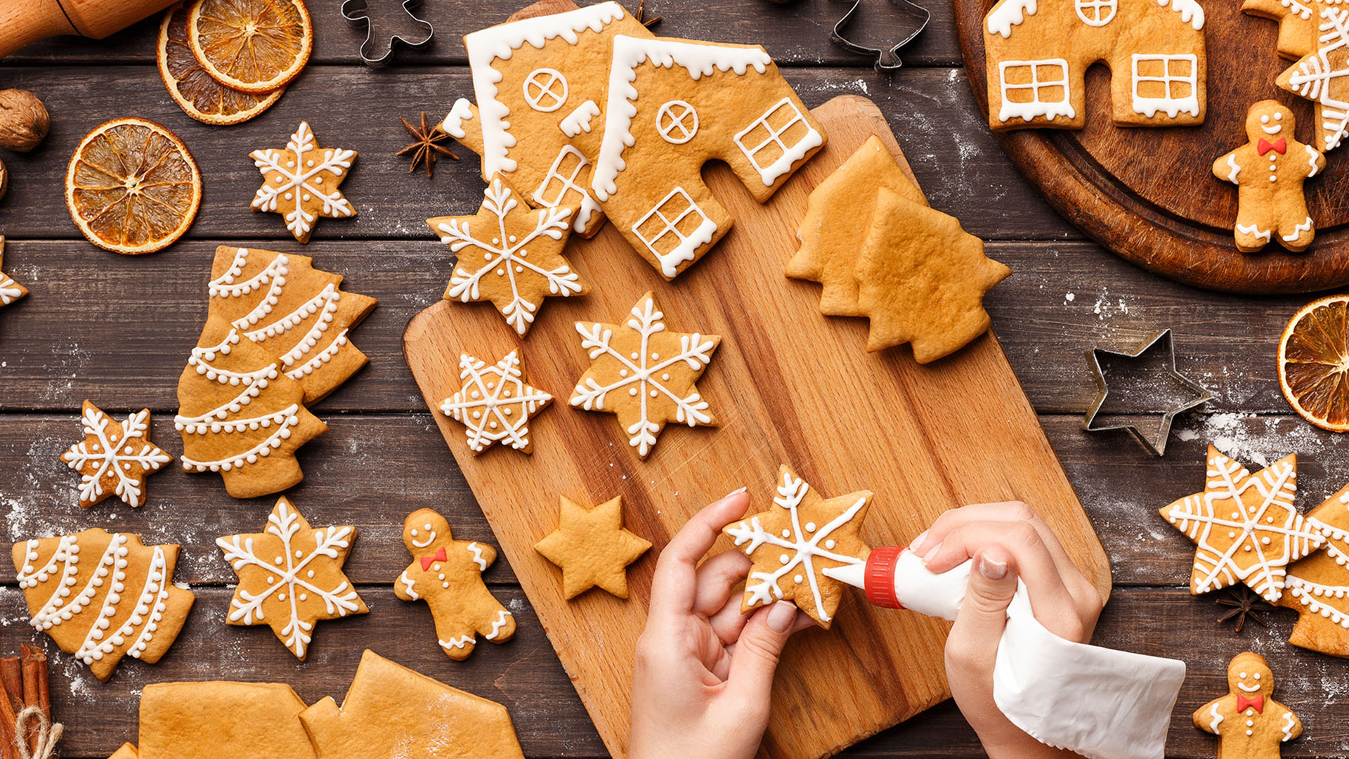 Icing process of Christmas bakery. Unrecognizable woman decorating homemade gingerbread cookies on wooden table, top view