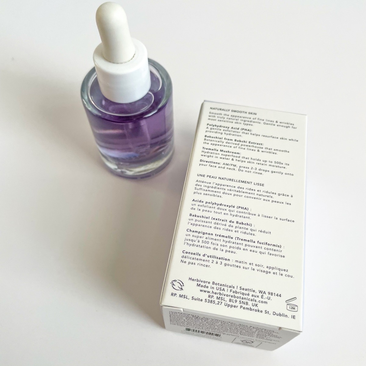 clear glass bottle of purple serum next to white box laying on its side