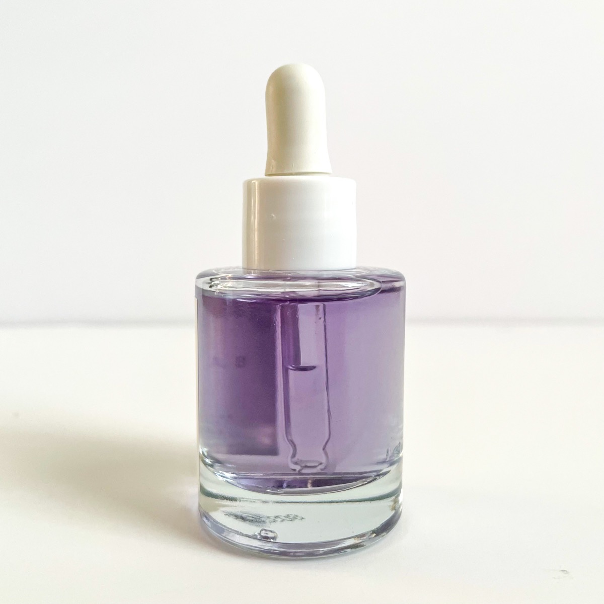 alternate view of clear glass bottle of purple serum