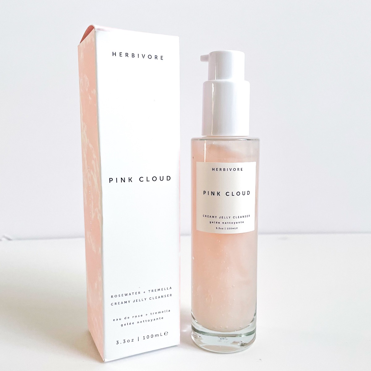 clear glass bottle of pink cleanser next to white box it came packaged in