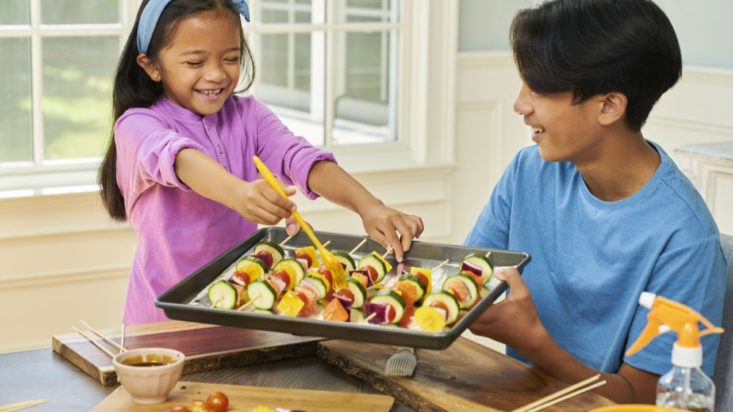 Photo of girl and boy holding tray of skewers