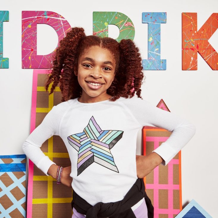 girl with hands on hips wearing shirt with star on it standing in front of kidpik logo