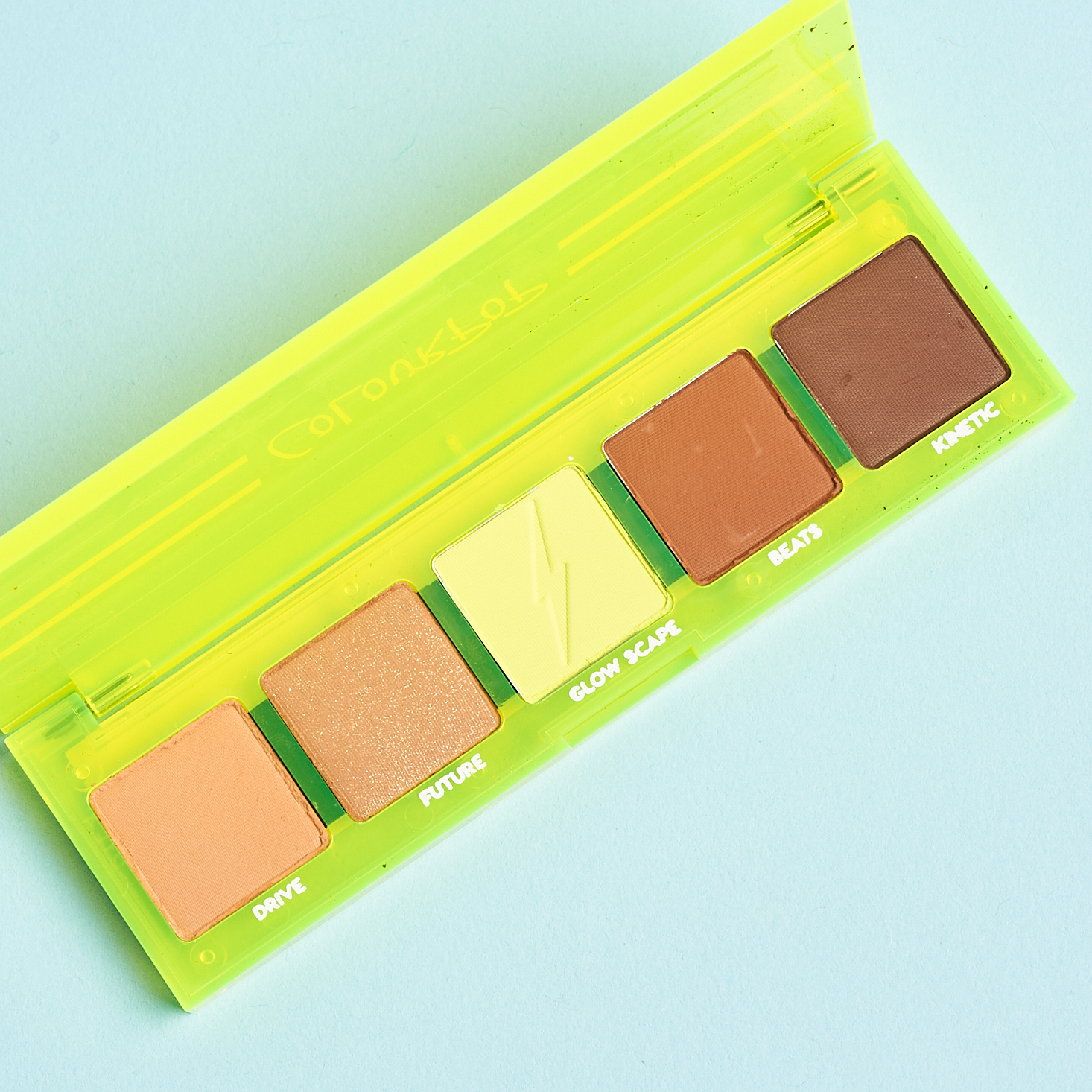 opened neon yellow plastic eyeshadow palette showing four brown shades and a neon yellow shade