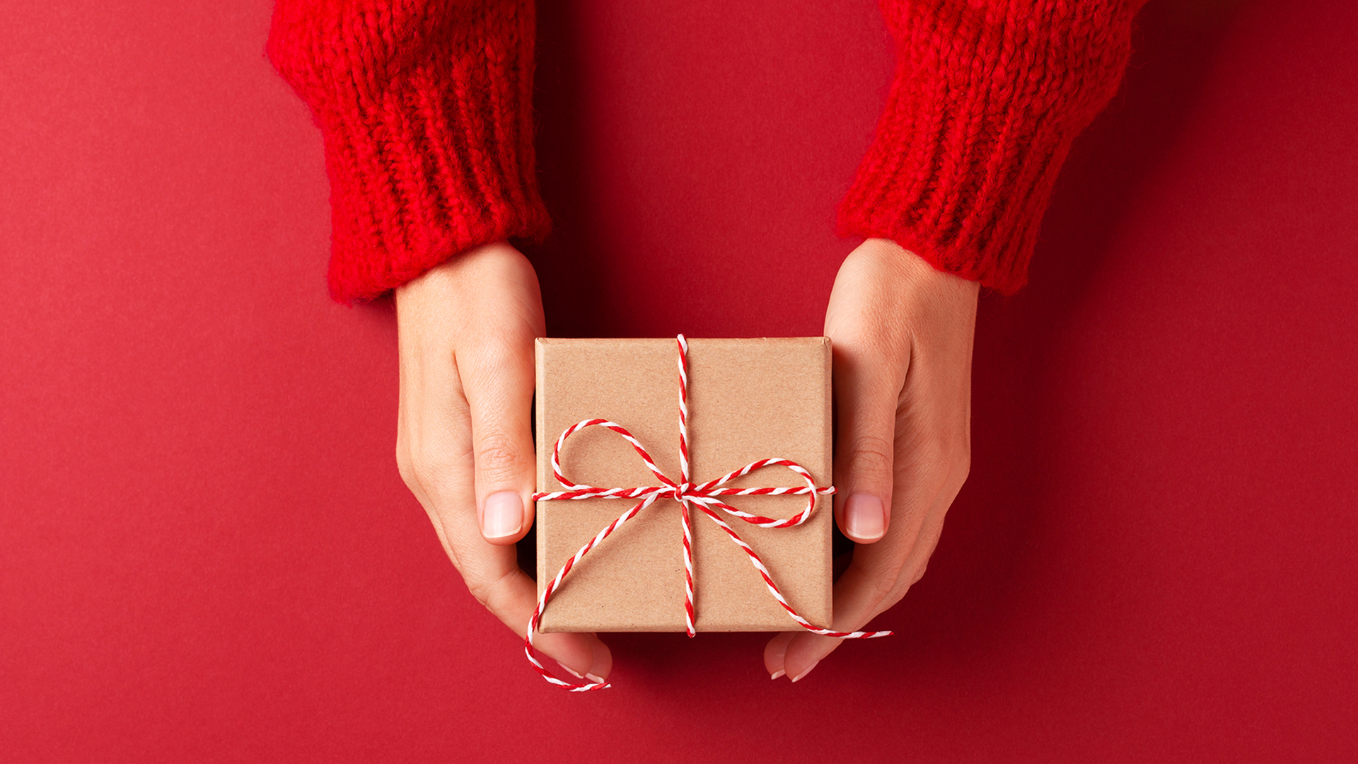 Female's hands in red pullover holding Christmas gift box on red background. Christmas and New Year concept.