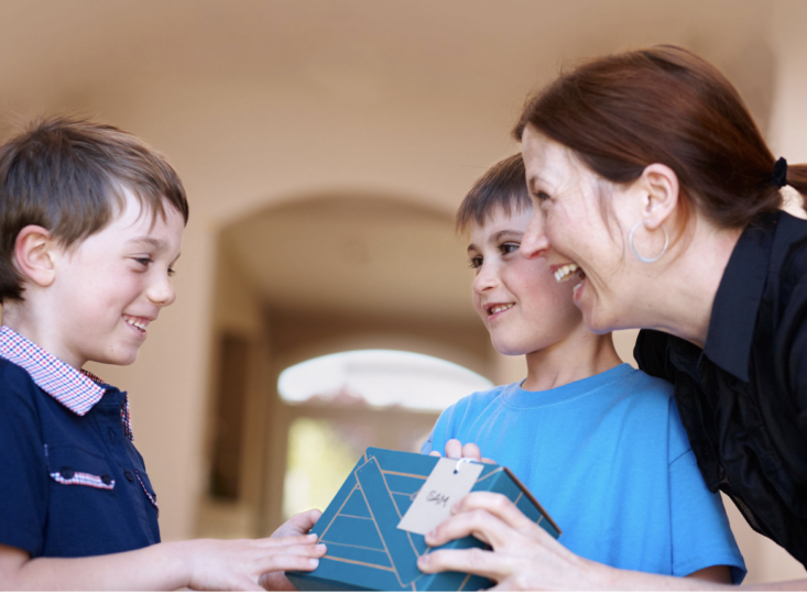 child giving another child a kiwico gift while mom looks on