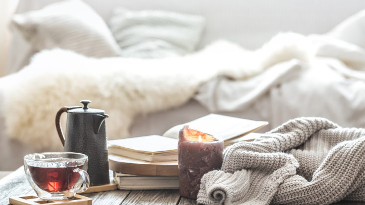 Still life home comfort in the living room with a Cup of tea and a kettle , near a burning candle and a knitted sweater.The concept of home atmosphere and comfort