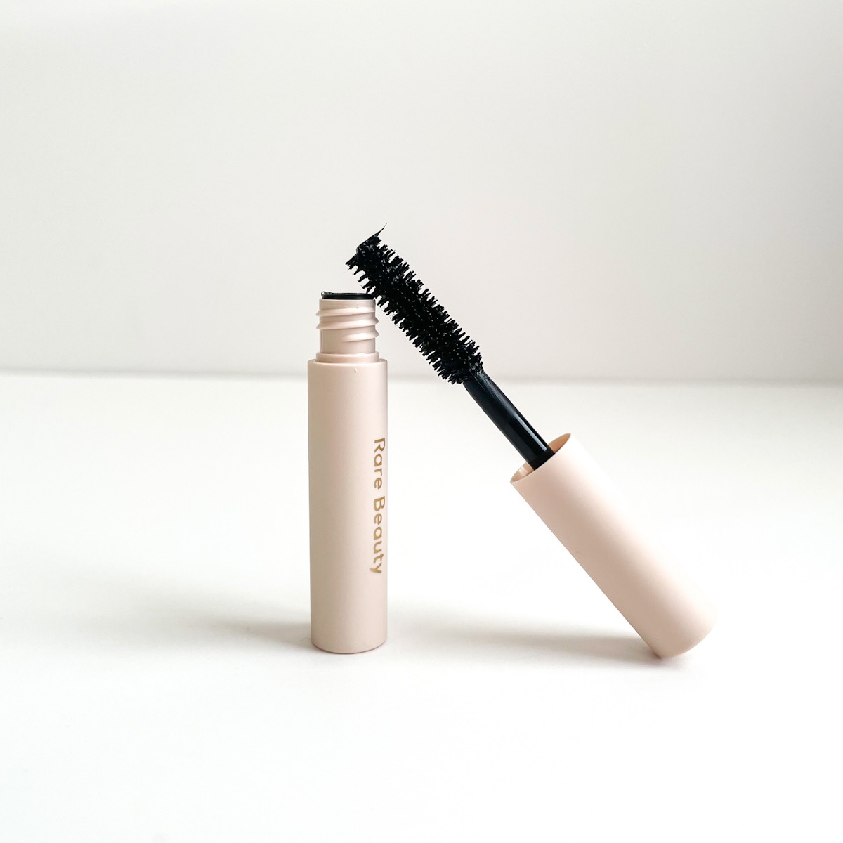 opened beige mascara tube with fluffy wand leaning against body of mascara