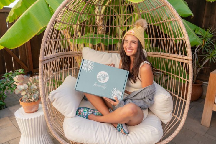 woman holding a beachly box while sitting in a big chair on the beach