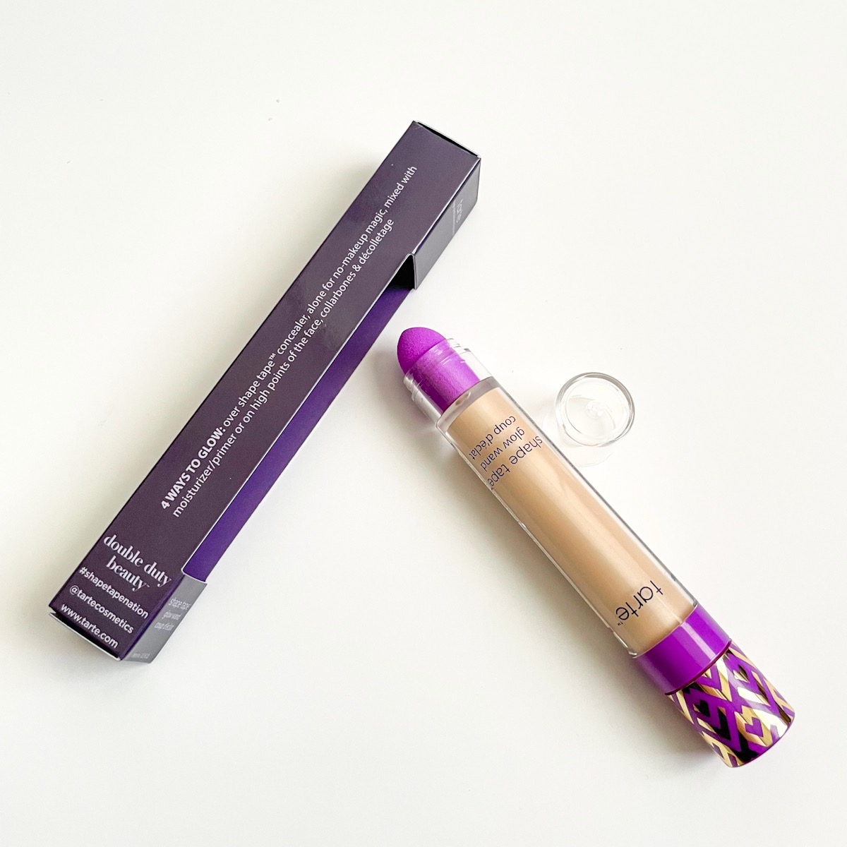 dark purple packaging on its side with highlighter wand laying next to it