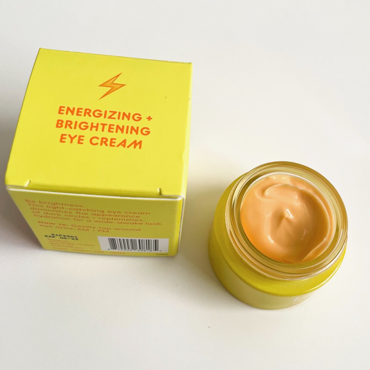 alternate view of yellow box next to opened yellow jar showing peach eye cream
