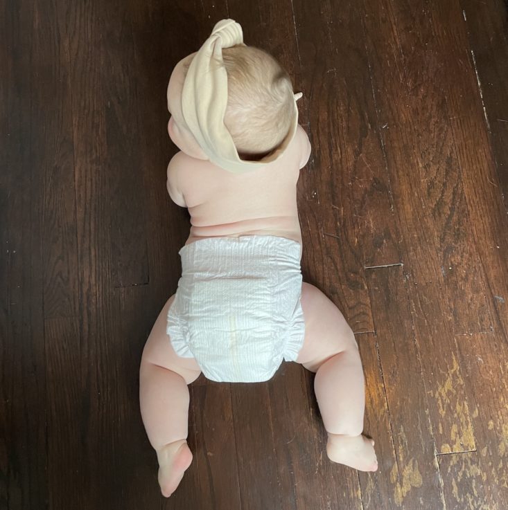 Baby on her tummy wearing headband and Coterie diaper.