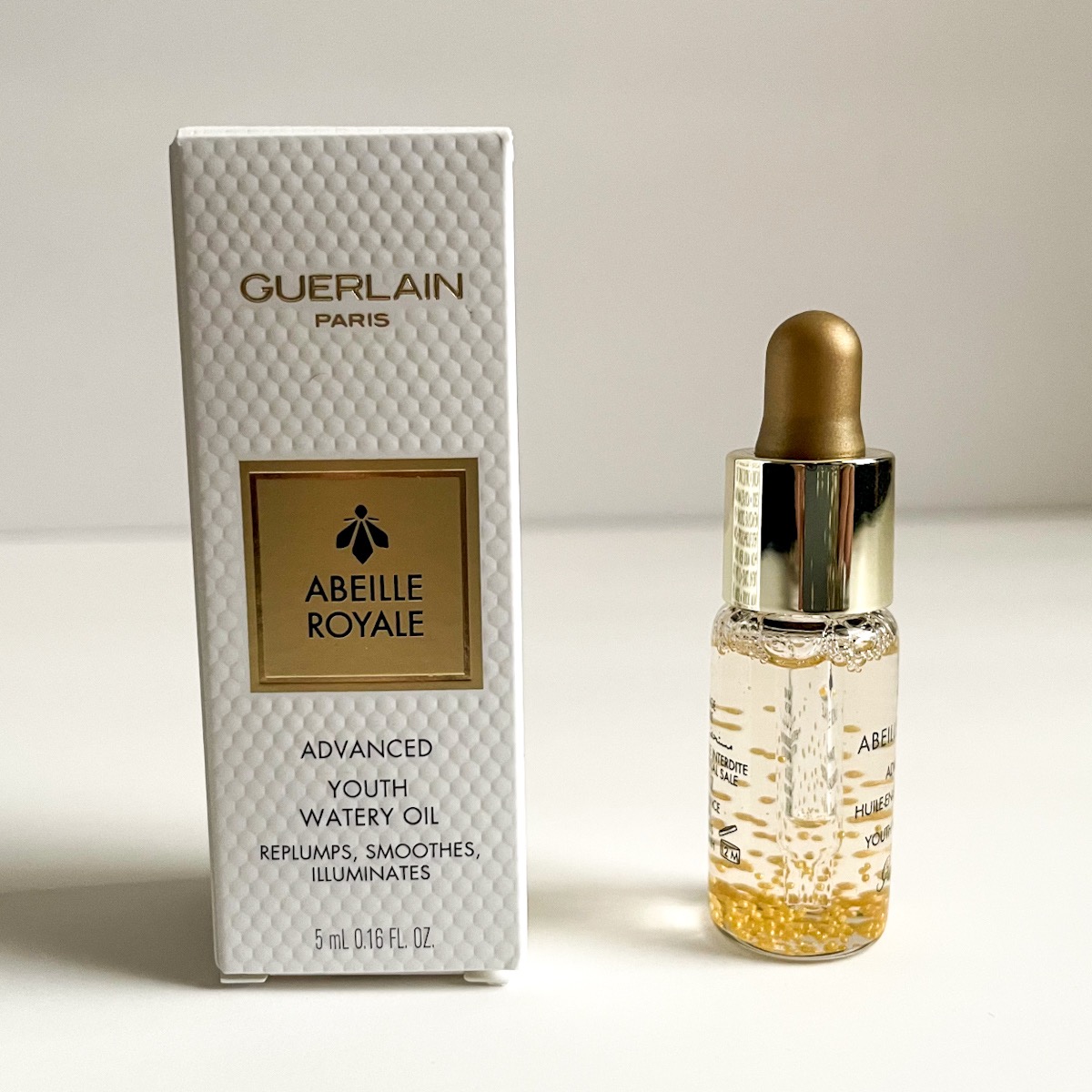 clear bottle of serum with little gold balls next to white and gold box