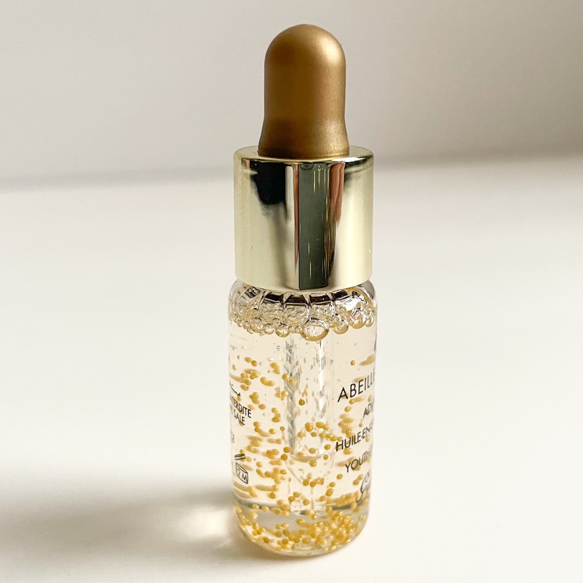 clear bottle of serum with gold lid and little gold balls