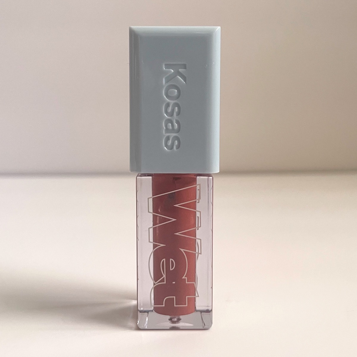 clear tube of lip gloss showing nude color and light blue lid