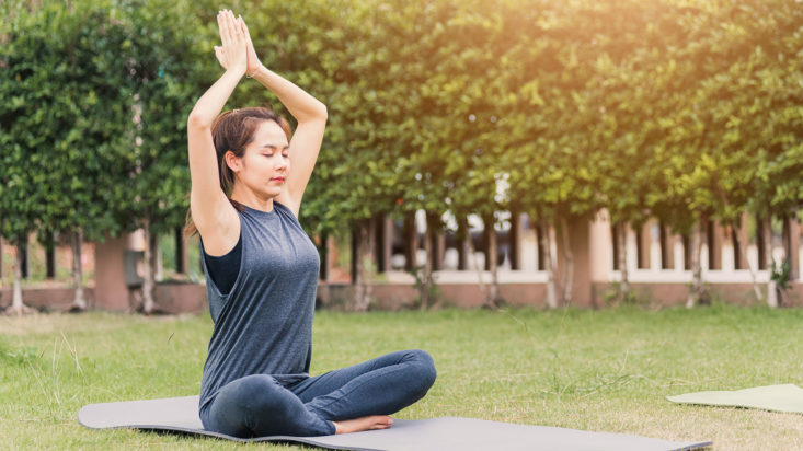 Young woman practicing yoga outdoors in meditate pose sitting on green grass with closed eyes in nature a field garden park, Stretching, meditation, exercise health care concept