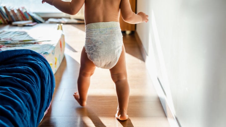 Baby in diapers learning to walk in her bedroom barefoot.