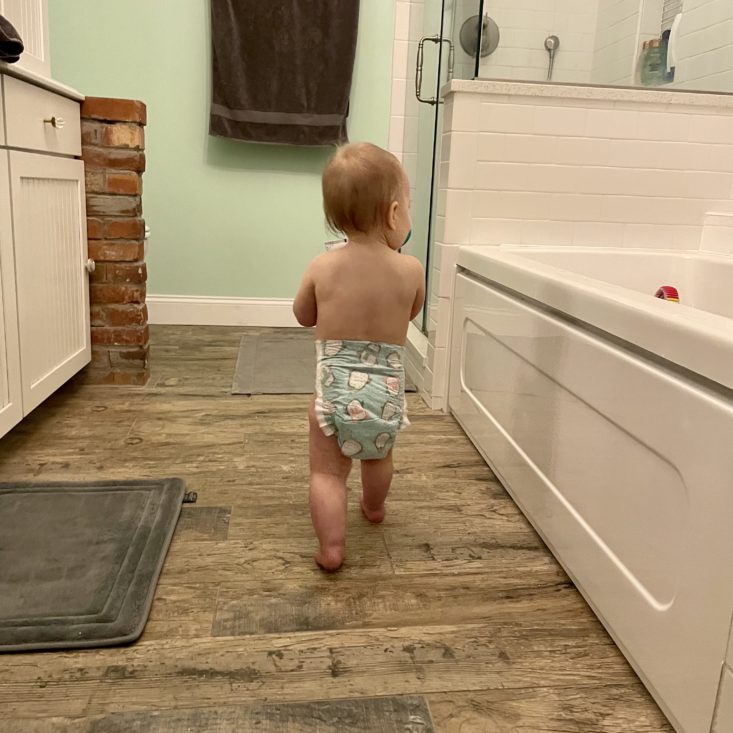 baby walking in the bathroom wearing a hello bello diaper.