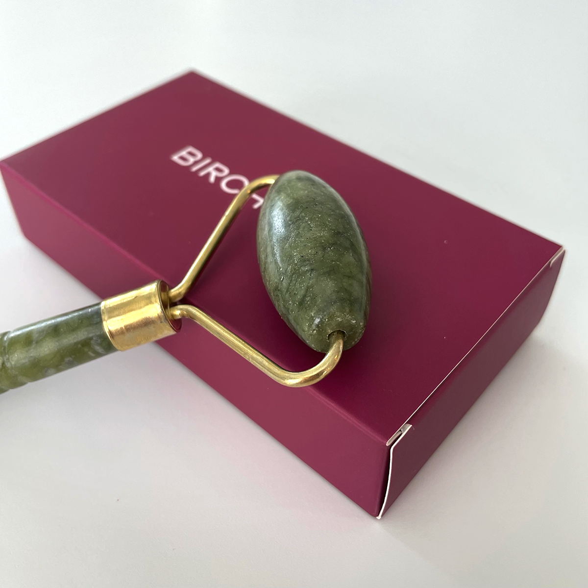 green jade roller laid on top of purple packaging box