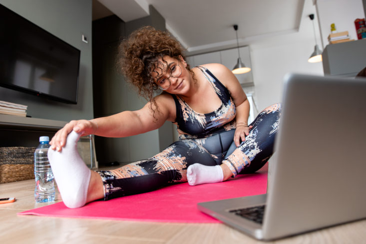 Young plus size woman at home doing exercise in front of open la