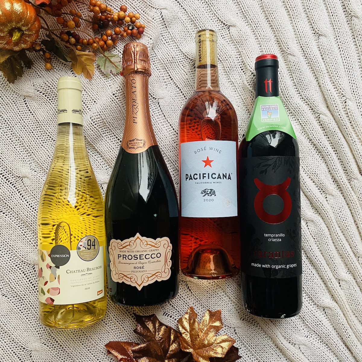 4 bottles of Winc wine displayed on a cream colored blanket near Fall floral decorations.