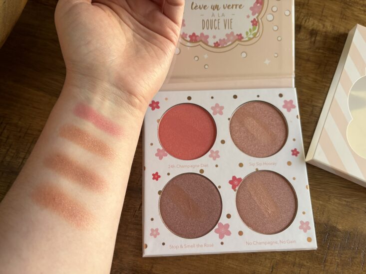 Beauty Bakerie Cotton Candy Champagne Blushlighter Palette open with four shades swatched on an arm, shades come in two pink hues and two orange hues