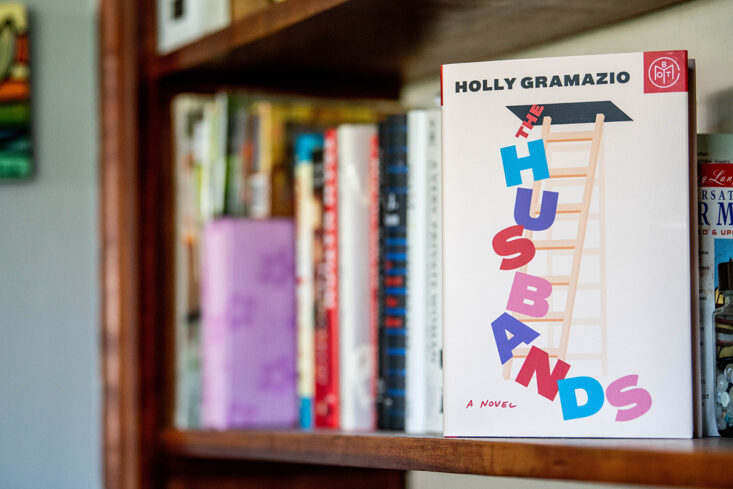 The book The Husbands by Holly Gramazio sits on a bookshelf